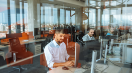 Office workers at modern open-plan desks using computers, with Remote-by-default service delivery